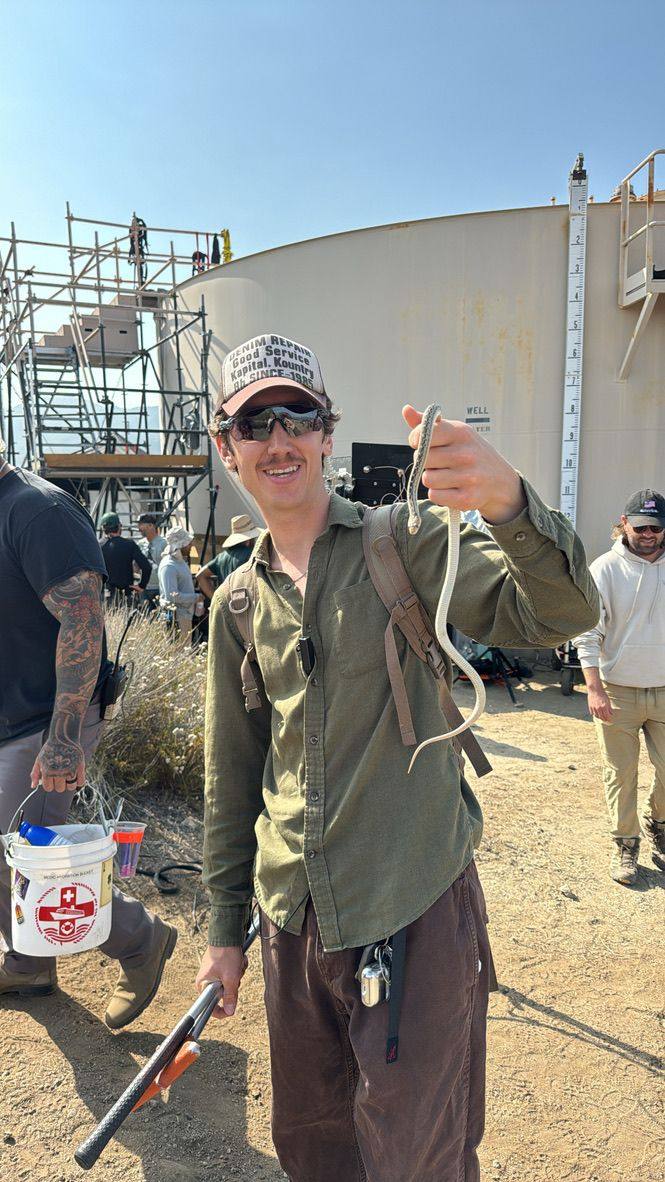 Derek Toth holding a juvenile gopher snake on set before relocating it